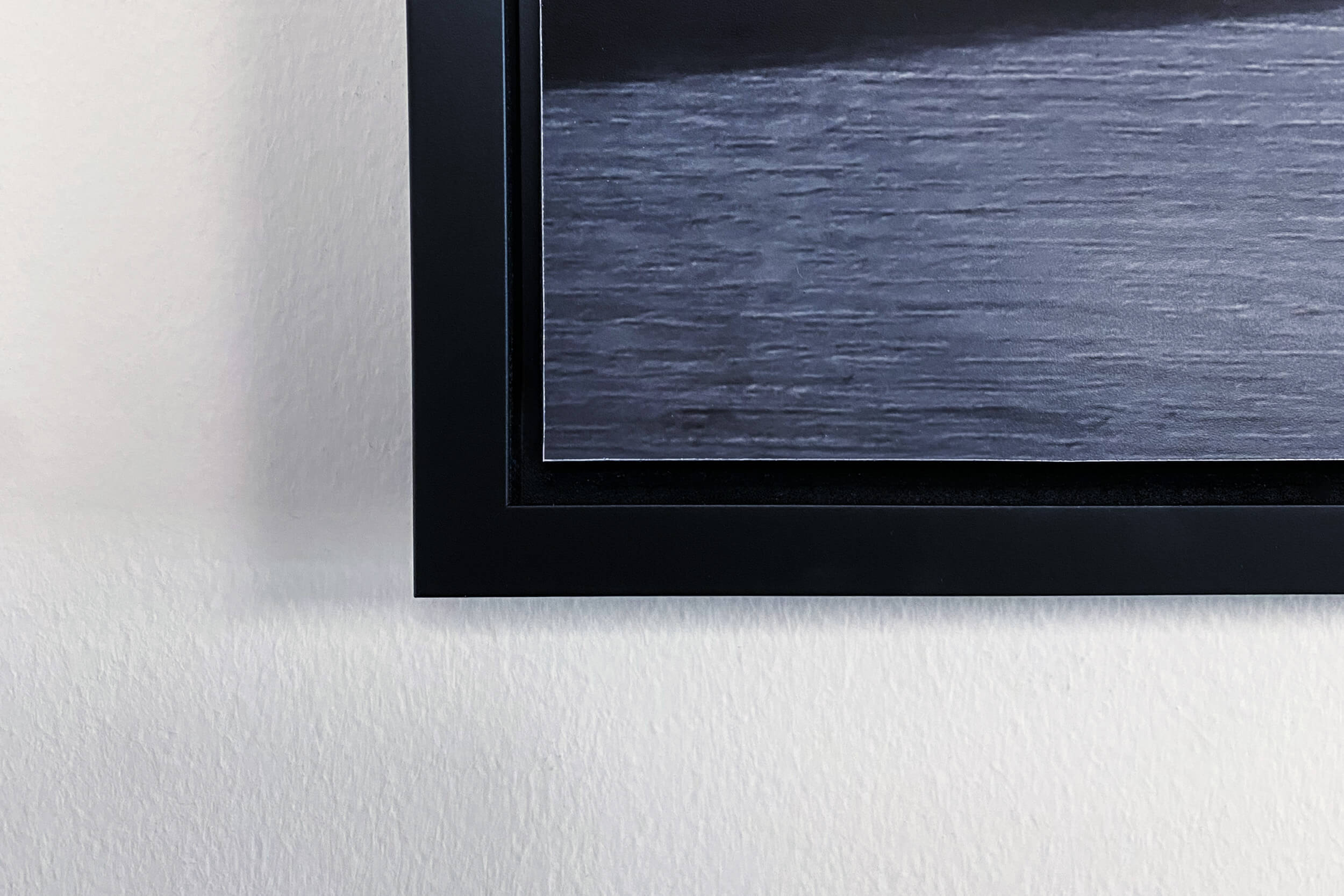 Corner detail of a black float frame on an acrylic print, showing the gap between the frame and the edge of the art
